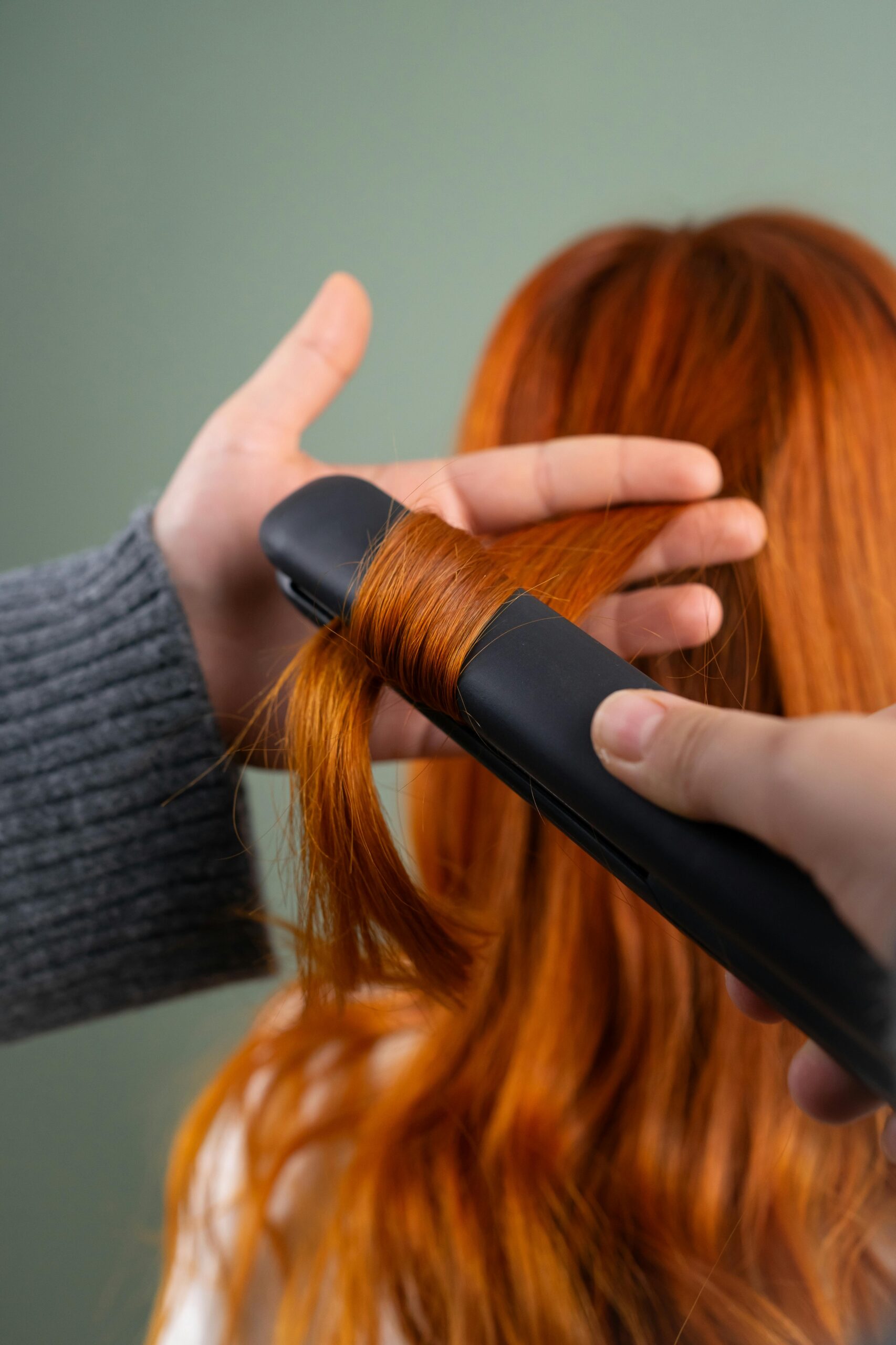 Close-up of red hair being styled with a flat iron indoors.