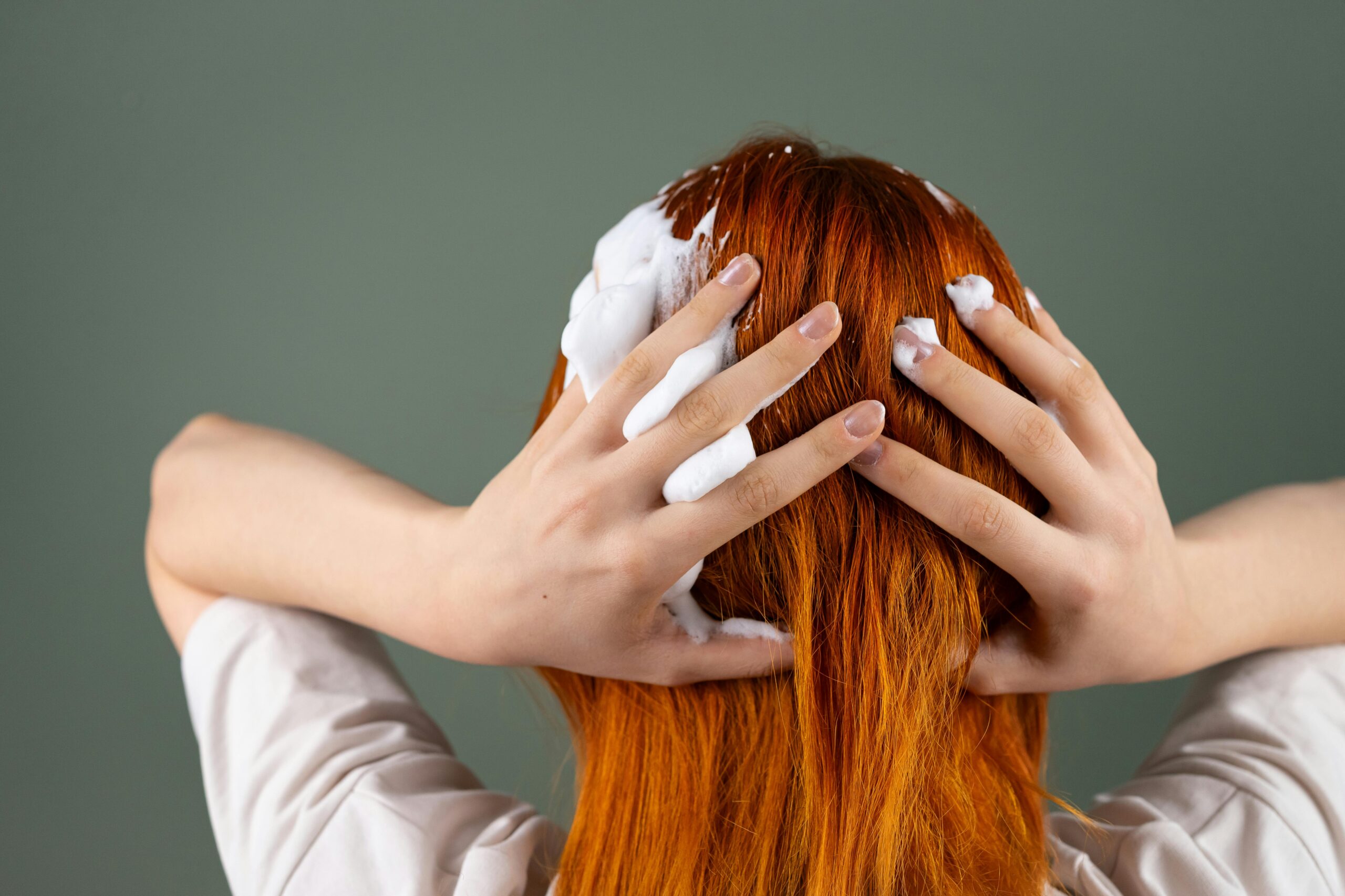 Back view of person washing red hair with shampoo in studio setting.