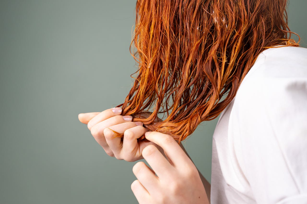 A detailed image showing a close-up of red hair being held by delicate hands against a neutral background.